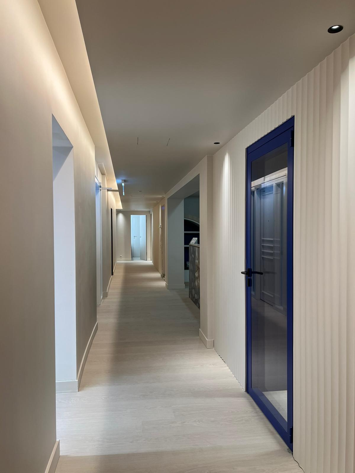 Couloir de circulation — porte verrière bleu Klein, mur cannelé blanc et éclairage indirect
