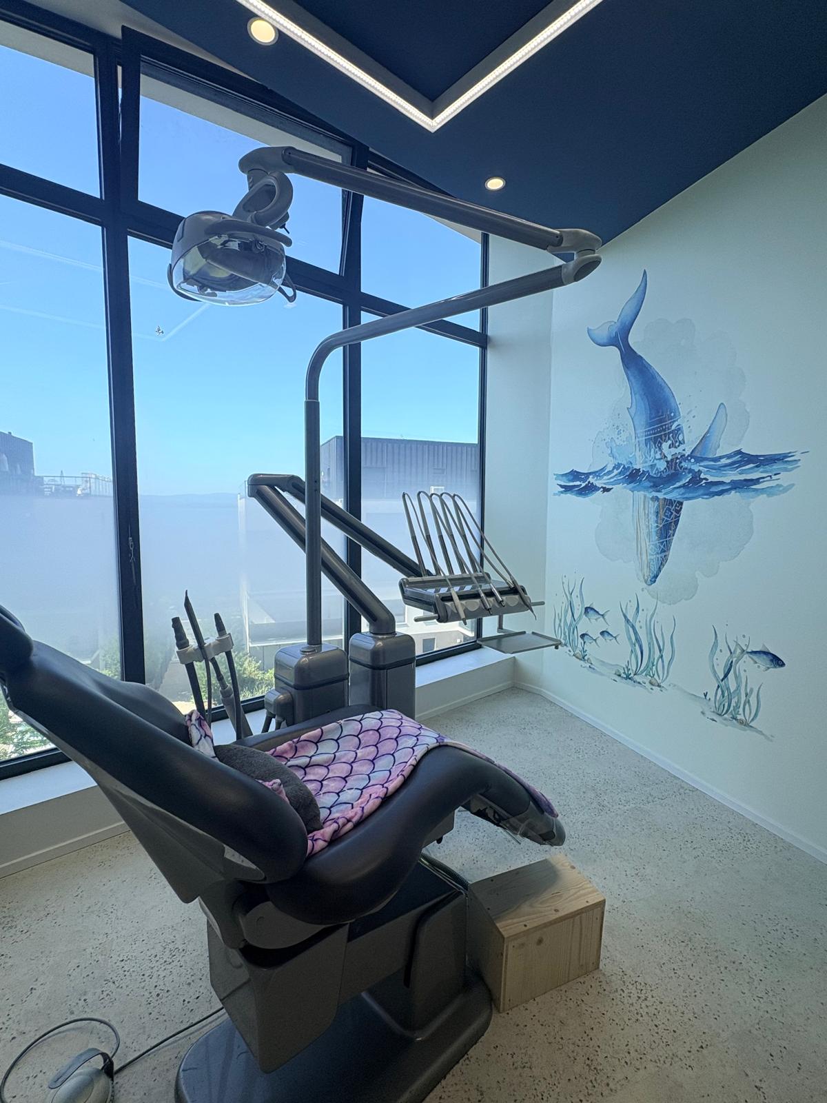 Salle de soin pédiatrique — fauteuil dentaire, plaid sirène et fresque baleine sur fond plafond bleu profond