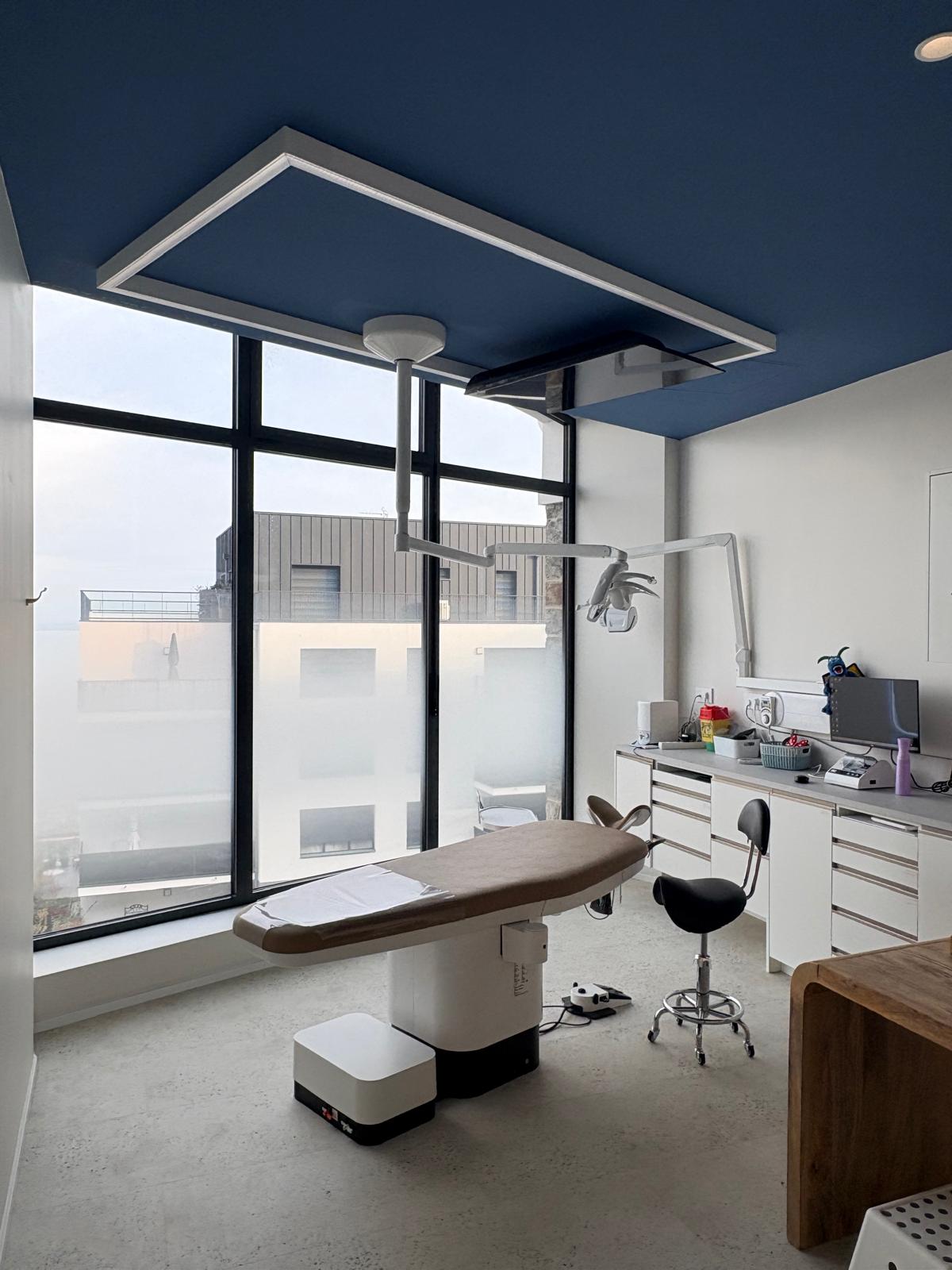 Salle de soin adulte — grande verrière, plafond bleu nuit encadré de néon lumineux et bureau de soin épuré