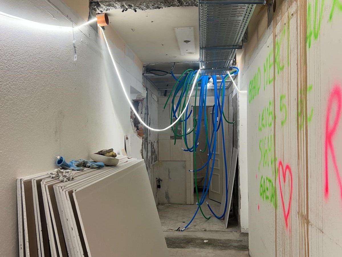 Avant chantier — couloir en travaux avec tags verts et roses, gaines et câbles apparents