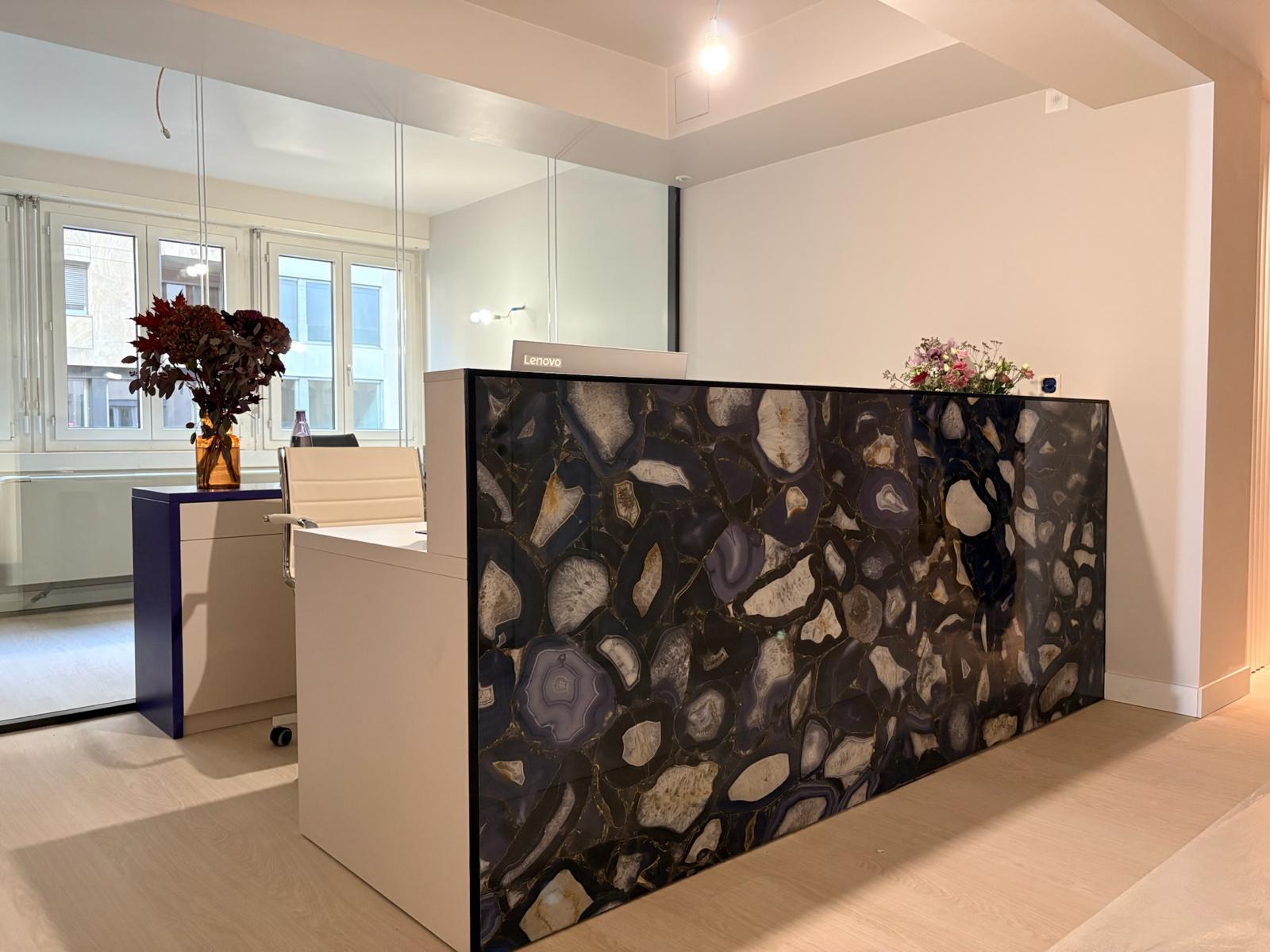 Accueil — banque agate noire rétroéclairée, vue d'angle avec bureau et bouquets